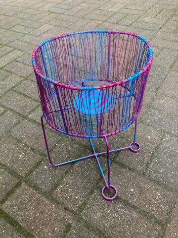 Close-up of a pink and blue woven-wire plant stand on a brick patio