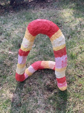 Looped sculpture striped in red, yellow, and pink, viewed from another angle
